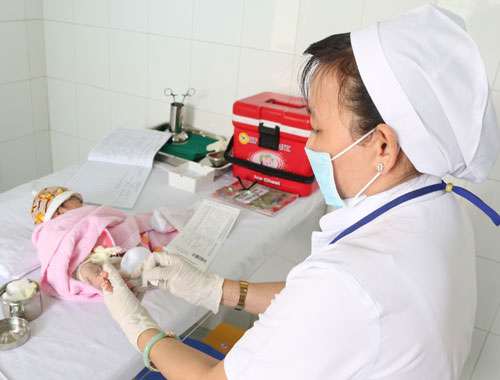 Cán bộ y tế thực hiện lấy máu gót chân xét nghiệm sàng lọc cho trẻ sơ sinh.